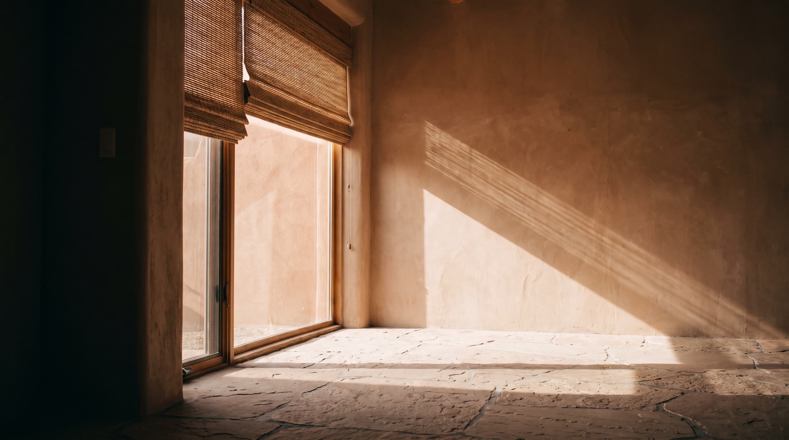 Low sun through a glass door, falling in bands across a plaster wall and a stone floor